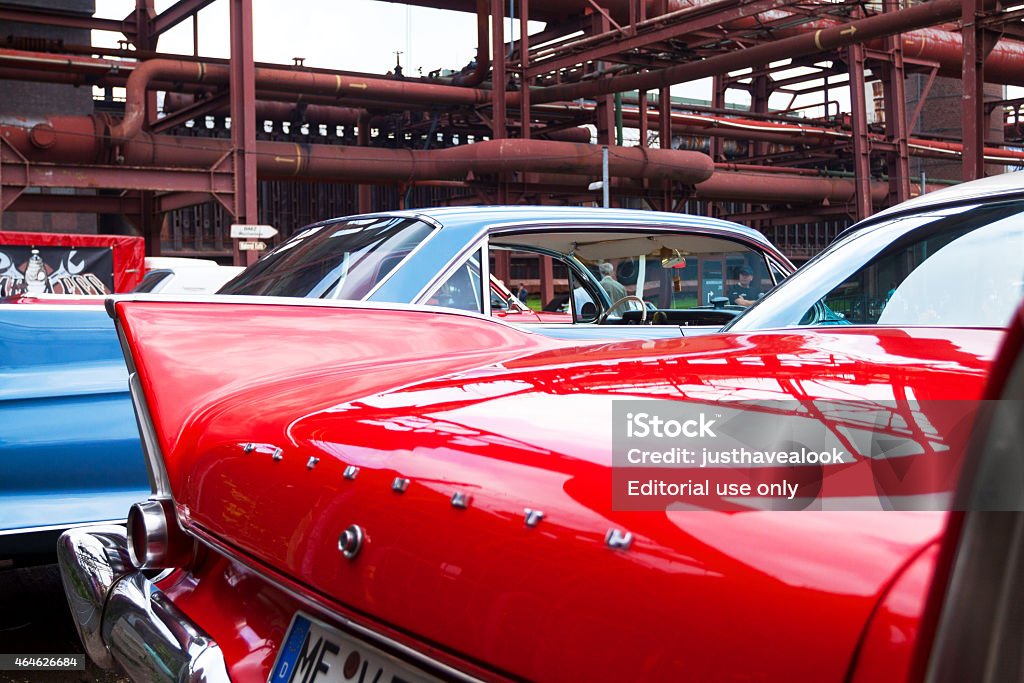 Cadillac oldtimers at Zeche Zollverein Essen, Germany - September 7, 2014: Capture of Cadillac Plymouth oldtimers standing at Zeche Zollverein in Essen at coke oven during oldtimer meeting. View over back and wings of red one to blue one in background. A man is passing in background. 2015 Stock Photo