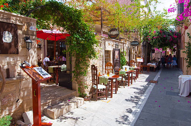Row of local restaurants. Rethymno old town. Crete. Greece. Crete, Rethymno, Greece - July 23, 2014: Row of  local restaurants on the shadow street invites guests with warm atmosphere, group of tourists have their meal inside the testaurant. herakleion photos stock pictures, royalty-free photos & images