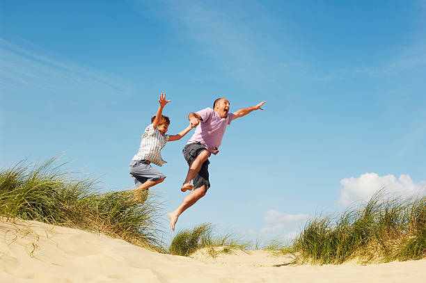 istock Father And Son Jumping On Sand At Beach 464628621
