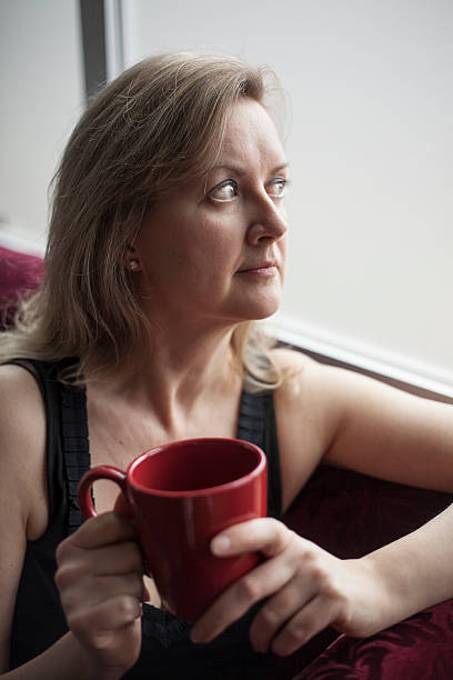 blonde femme avec rouge tasse à café, assis près d'une fenêtre - the human body photos photos et images de collection