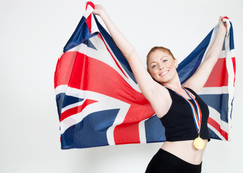 A beautiful young woman wearing a gold medal and holding up a British flag.  Shot in the studio.