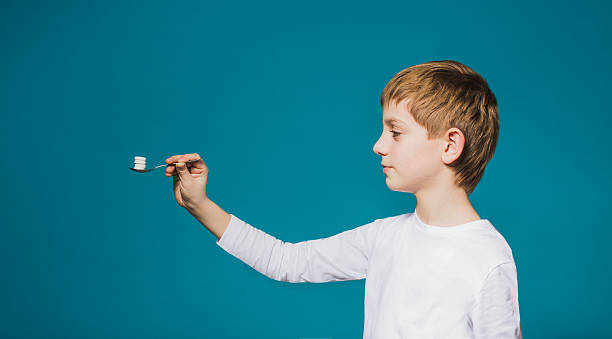 istock Boy in white clothes holding spoon with pills 464640332