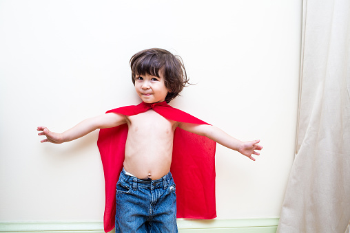 Little boy with outstretched arms with a red cape pretends to fly