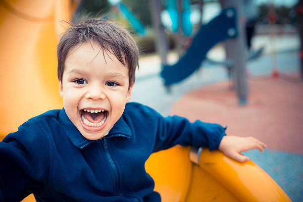 Cute boy happily playing on a playground slide A cute young mixed race Asian Caucasian boy plays happily on a yellow slide in an outdoor playground. live boy stock pictures, royalty-free photos & images
