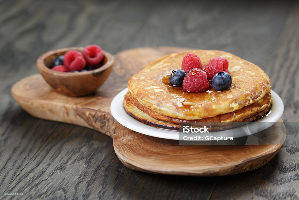 Pancakes pictures with a topping of berries and maple syrup Pancakes with raspberry, blueberry and maple syrup, on oak wooden table 2015 Stock Photo