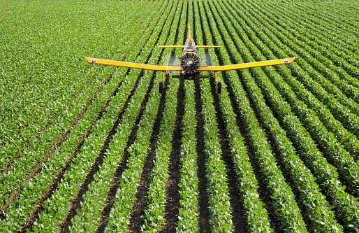 Unique perspective of an Aerial Sprayer Airplane flying low over a farmer’s field applying pesticides on the crops.  All logos have been removed.