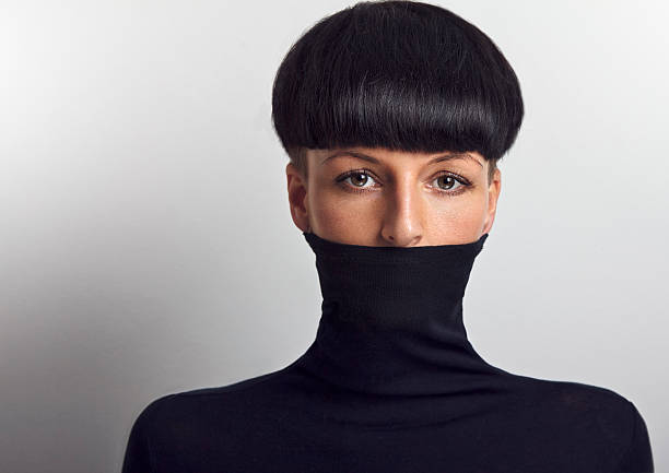 Beautiful woman with black mushroom hair cut covering her face with black turtleneck looking at the camera. Developed from RAW. Retouched with special care and attention. Small amount of grain added for best final impression. Adobe RGB color profile.