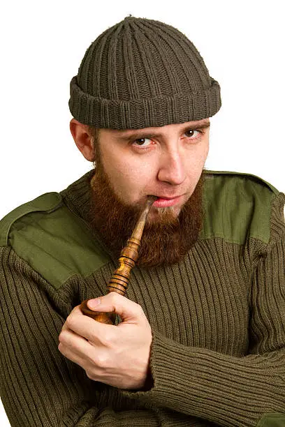 young bearded guy smoking a pipe on a light background
