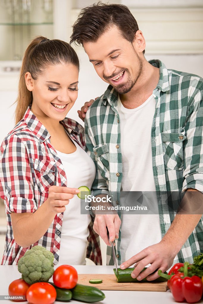 Kitchen Beautiful young couple in the kitchen while cooking.Smiling woman and  husband are cooking with fresh vegetables. Adult Stock Photo