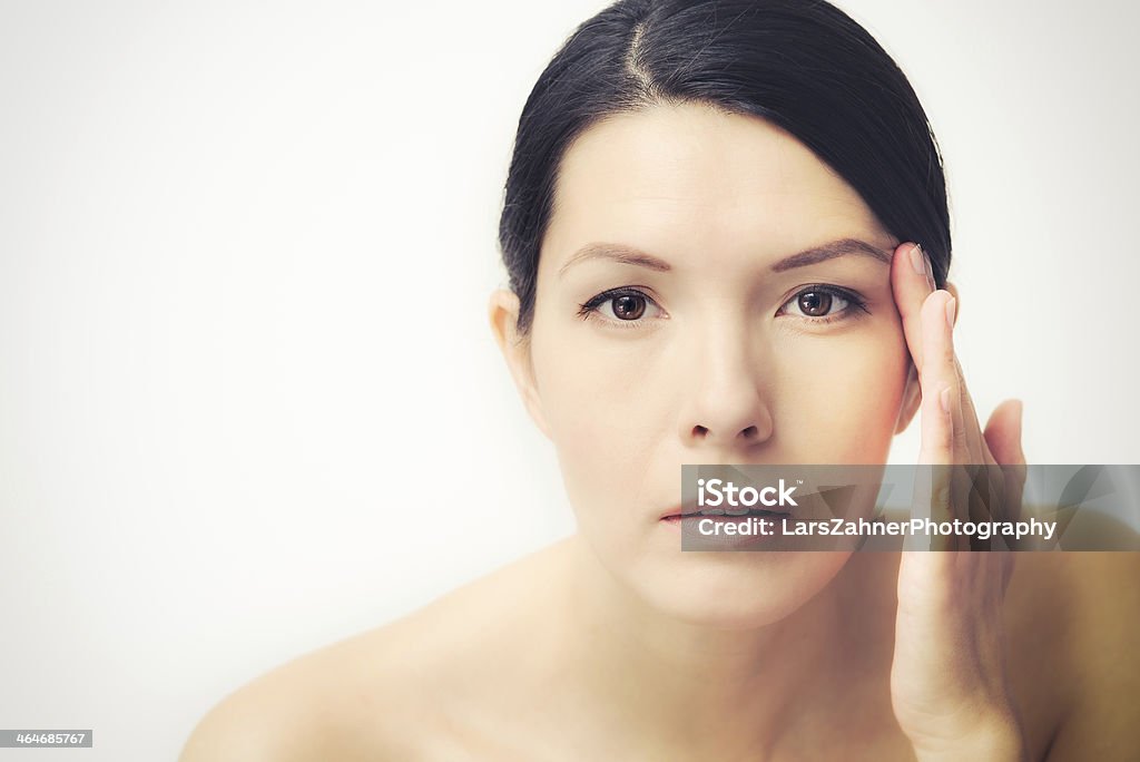 Young woman observing facial wrinkles Portrait of a sexy brunette Caucasian young woman looking in the mirror, observing facial wrinkles, first sign of ageing Human Face Stock Photo