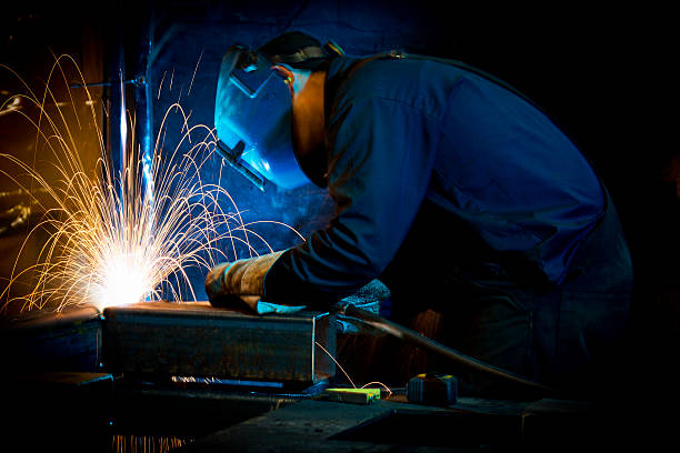 Welder leaning over a fabricating task while sparks fly A welder fabricating structural steel structural steel stock pictures, royalty-free photos & images