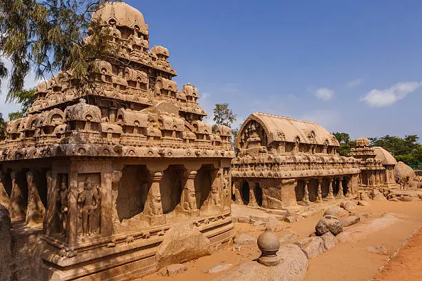 Four of the Pancha, or Five Rathas (also known as Pandava Rathas) lined up in the sun at Mahabalipuram, on the Coromandel Coast of the Bay of Bengal, in the state of Tamil Nadu, India. Dating from the late 7th century, they are attributed to the reign of King Mahendravarman I and his son Narasimhavarman I (630–680 AD) of the Pallava Kingdom. Photo shows, from the left, the Dharmaraja, Bhima, Arjuna and Draupadi Rathas. The structures are without any precedence in Indian temple architecture and are completely carved out of a single rock each. They withstood the ravages of the Tsunamis of the 13th Century and 2004. They however display the effects of wind and sand erosion. These are not temples as they are unfinished and were never consecrated. They are part of the UNESCO World Heritage site at Mahabalipuram. Photo shot in the afternoon sunlight; no people.  Horizontal format. Copy space. Camera: Canon EOS 5D MII; Lens: Canon EF24-70 f2.8L