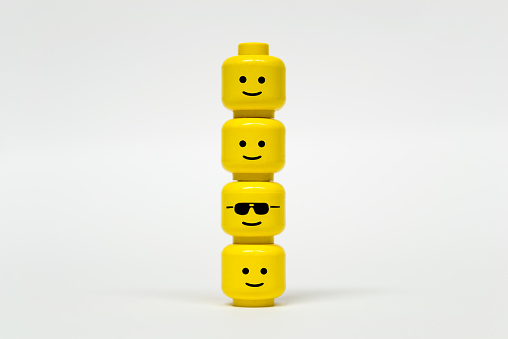 Florence, Italy - February 24, 2015: Lego mini figure heads being in series with one different head with glasses. All of faces are smiling.