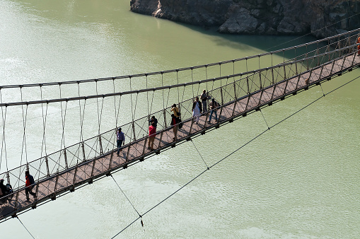 Rishikesh, India - December 9, 2014:  Laxman Jhula bridge over Ganges river.  People crossing footbridge. Rishikesh is  World Capital of Yoga,  has numerous yoga centres that also attract tourists