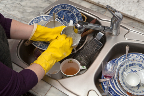 Hands in yellow gloves wash the dirty dishes in the sink silver