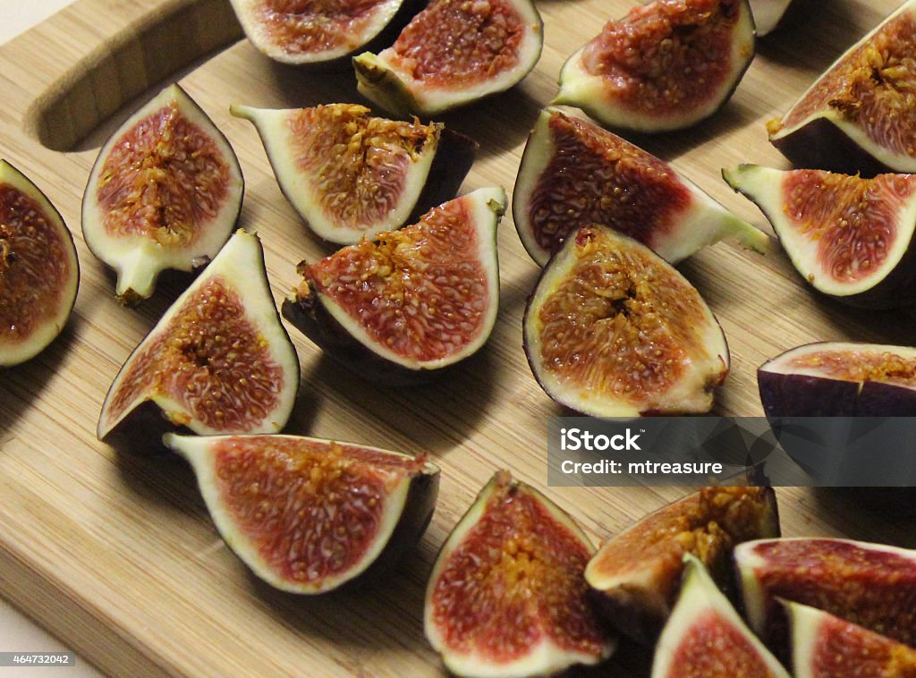 Image of sliced fresh figs on wooden breadboard, party food Close-up photo showing a large group of fresh figs, sliced in half and displayed on a wooden breadboard, next to some cheeses and green grapes.  The figs are part of a selection of help-yourself buffet food at a party.  Of note, this particular fruit / plant variety is known in Latin as: Ficus carica. 2015 Stock Photo