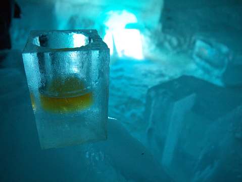 Frozen Shot glass with whiskey made of ice, shaped form frozen water in dark blue ice bar environment