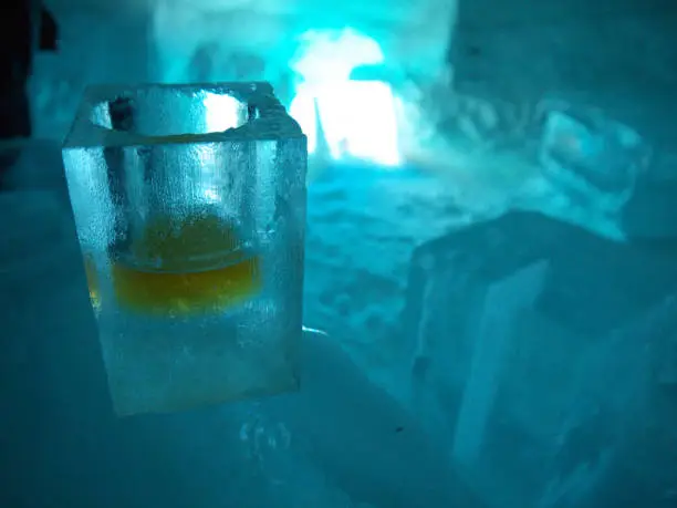 Frozen Shot glass with whiskey made of ice, shaped form frozen water in dark blue ice bar environment