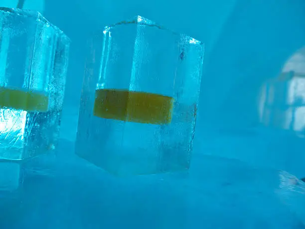Two Frozen Shot glasses with whiskey made of ice, shaped form frozen water in dark blue environment on ice bar