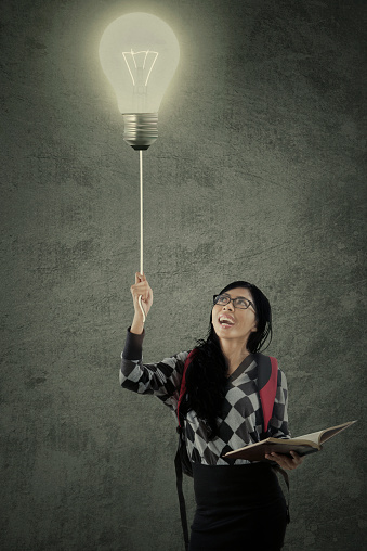 Female college student holding a book and turn on the light in the classroom with a blackboard background