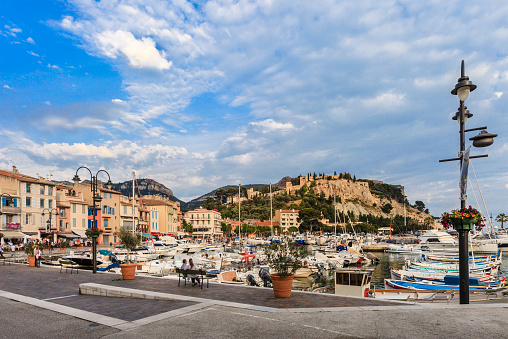 Cassis, France - June 4, 2014: People relaxing at the harbor in the small town of Cassis, where numerous restaurants face the sea offering a typical cuisine. On the top of the rocky cliff stands a castle,  converted into a luxury hotel.