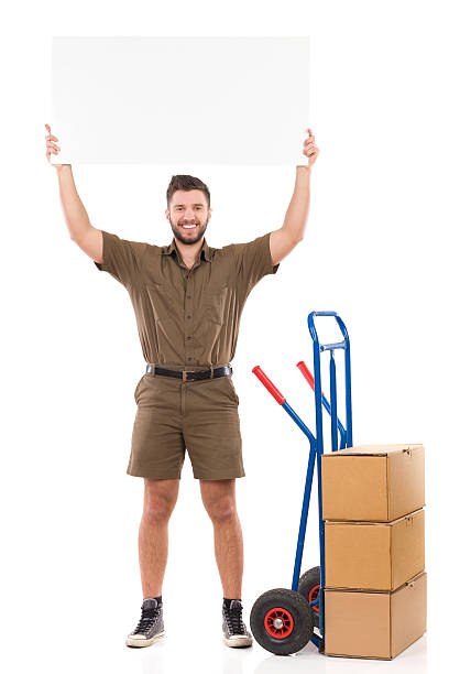 Free Shipping Day Happy delivery man standing and holding a blank banner over his head. Full length studio shot isolated on white. mover delivery person box hand truck stock pictures, royalty-free photos & images