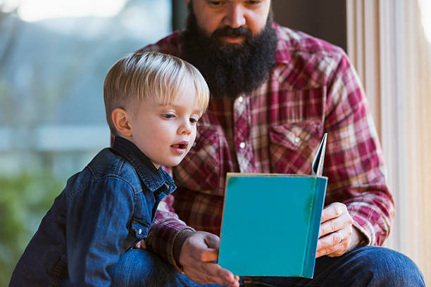 маленький мальчик с отцом, читая книгу - brown hair caucasian little boys men стоковые фото и изображения