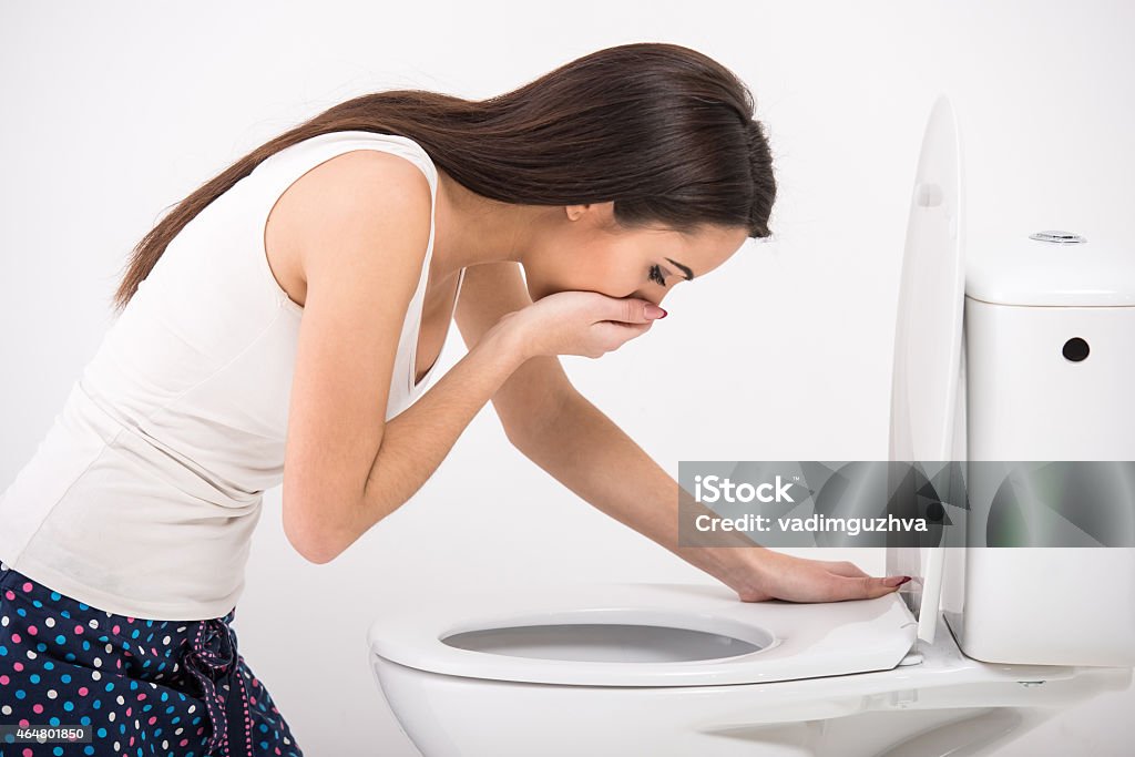 Woman in pajamas about to vomit into a toilet Young woman vomiting into the toilet bowl in the early stages of pregnancy or after a night of partying and drinking.Close-up of woman on toilet in morning. Bulimia Stock Photo