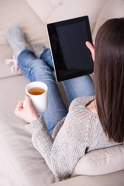 istock A woman sitting on a couch with a tablet and a coffee 464802412