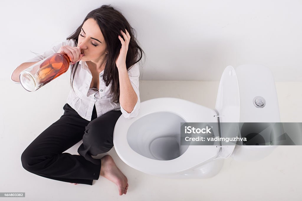 Woman in toilet Young woman in depression, is drinking alcohol in toilet.Young woman in depression, is drinking alcohol in toilet. 2015 Stock Photo