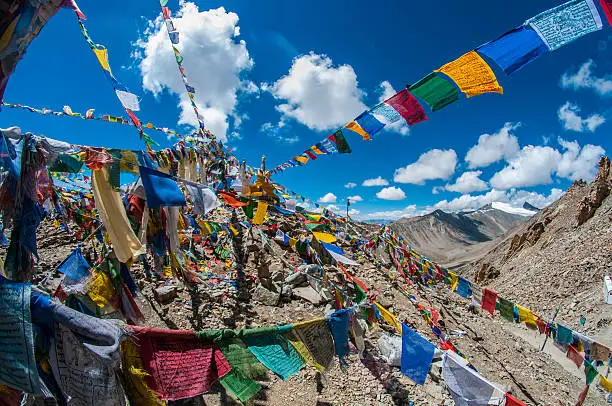 The shrine on top of Khardungla Pass; the highest motorable road in the World. Shot with a fisheye lens with bright coloured "Lung ta" or prayer flags against the blue sky and the mountain range in the back. Ladakh, India.
