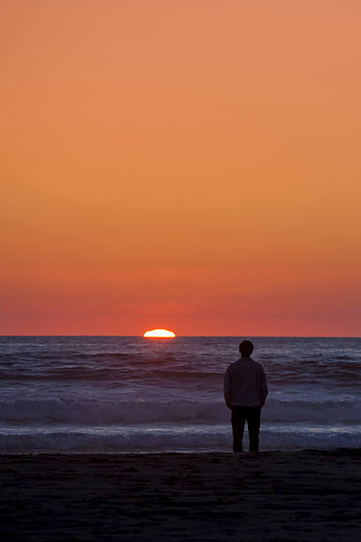 Man watching sunset over the ocean stock photo