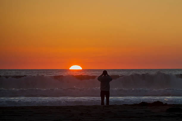 Man photographing sunset over the ocean stock photo