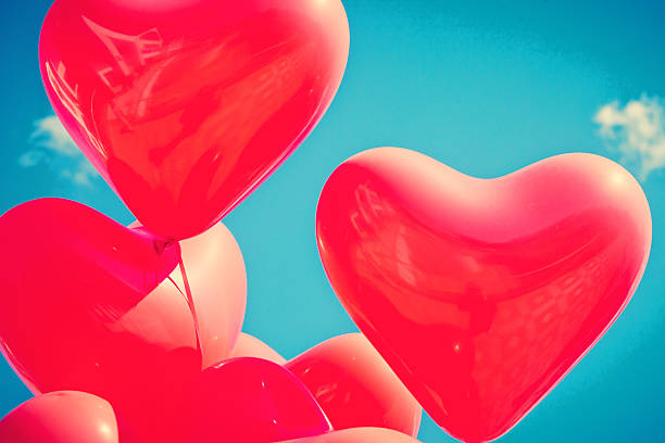 Flying heart shaped balloons in a clear sky stock photo