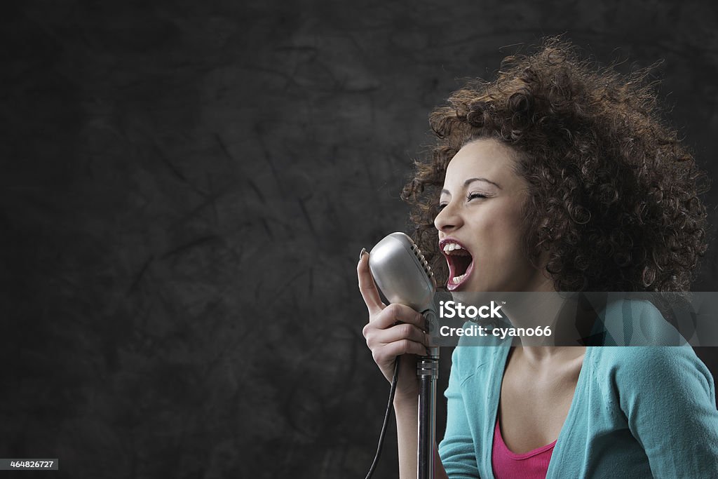 Young curly haired woman yelling into old school microphone Young female singer with brown curly hair singing a song Adult Stock Photo