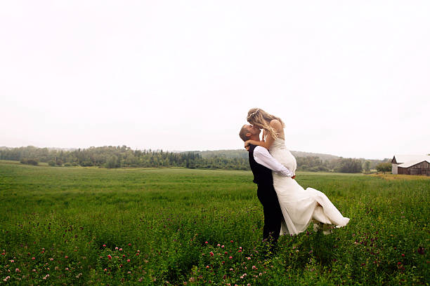 Bride and Groom Kissing in a Meadow A groom gives his bride a romantic kiss in a meadow of wildflowers.  real wife stories stock pictures, royalty-free photos & images