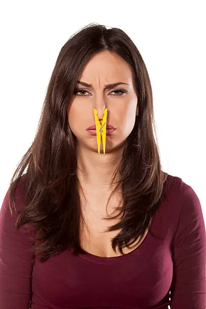 disgusted young woman pinching her nose with a clothespin