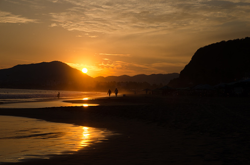 A fisherman and a couple walking along the beach sihouetted by the sunset on Miramar Beach in Colima Mexico