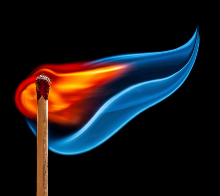 Close-up of igniting matchstick against coloured background.