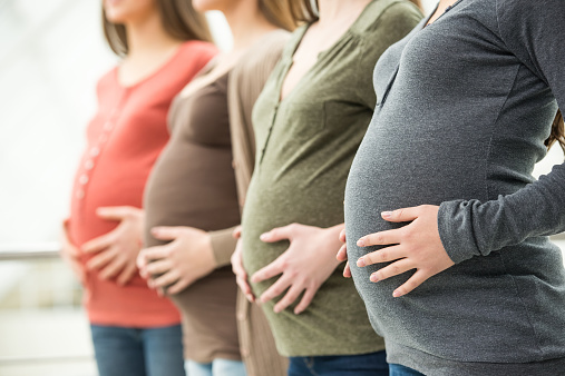 Side view of three pregnant women are touching their bellies with hands. Maternity concept.