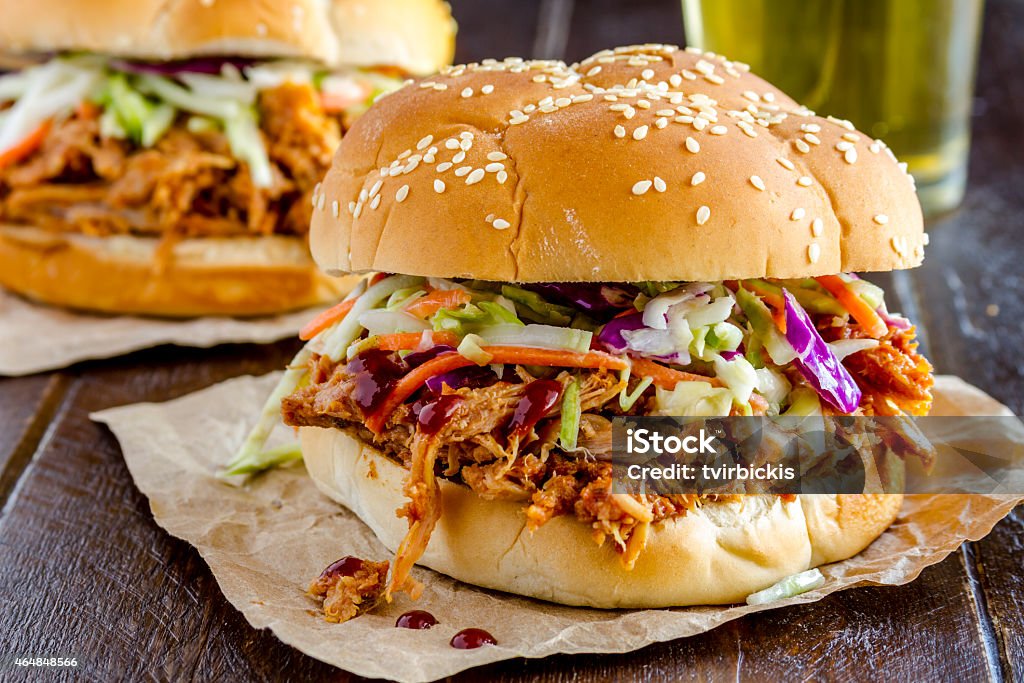 Barbeque Pulled Pork Sandwiches Close up of pulled pork barbeque sandwich with coleslaw sitting on wooden table with glass of beer Pulled Pork Stock Photo