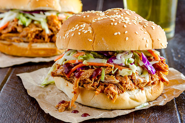 Barbeque Pulled Pork Sandwiches Close up of pulled pork barbeque sandwich with coleslaw sitting on wooden table with glass of beer coleslaw stock pictures, royalty-free photos & images