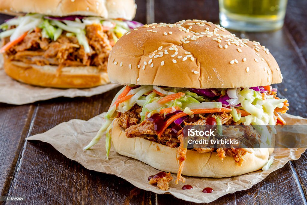 Barbeque Pulled Pork Sandwiches Two pulled pork barbeque sandwiches with coleslaw sitting on wooden table with glass of beer 2015 Stock Photo