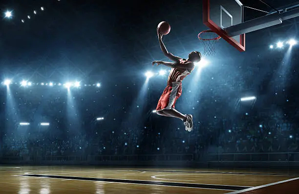Close up image of professional basketball player about to do slam dunk during basketball game in floodlight basketball court