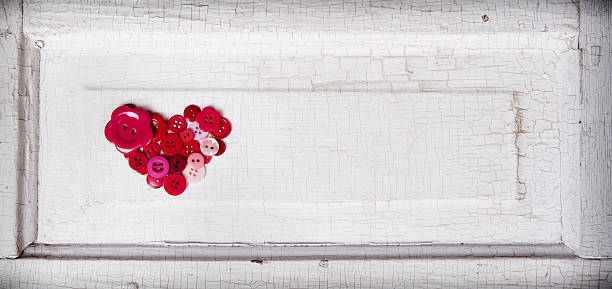 Sewing buttons in the shape of a heart on an antique wooden background