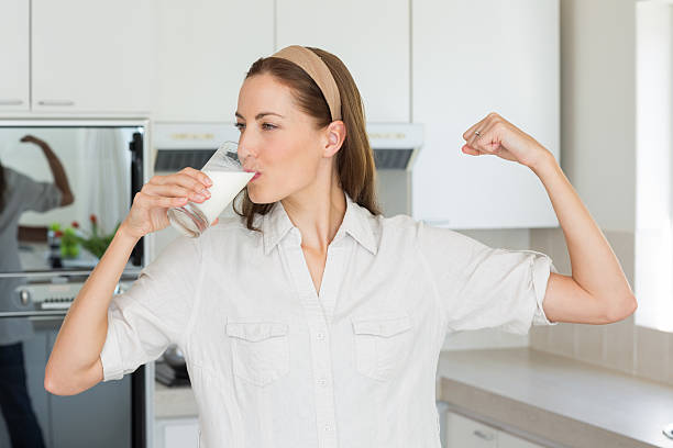 mujer flexionar los músculos mientras bebe leche en la cocina - mujer bebiendo leche fotografías e imágenes de stock