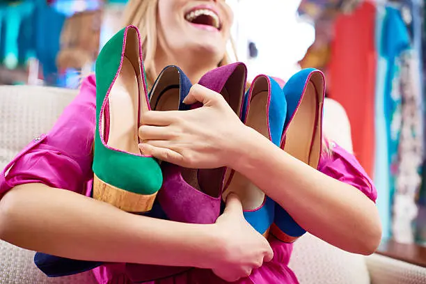 Female shopaholic with armful of multi colored high heels shoes