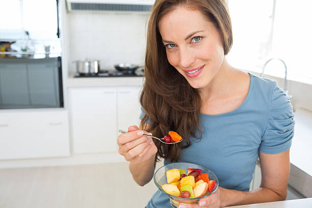 istock Smiling young woman eating fruit salad in kitchen 464865882