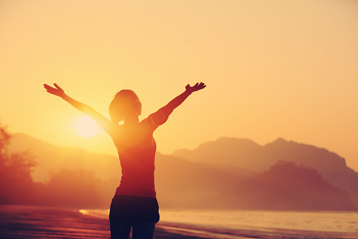 cheering woman open arms to sunrise at seaside