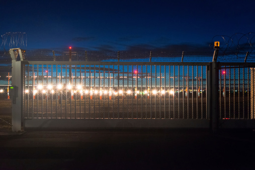 security fence around airport with runway lights in the background at dusk